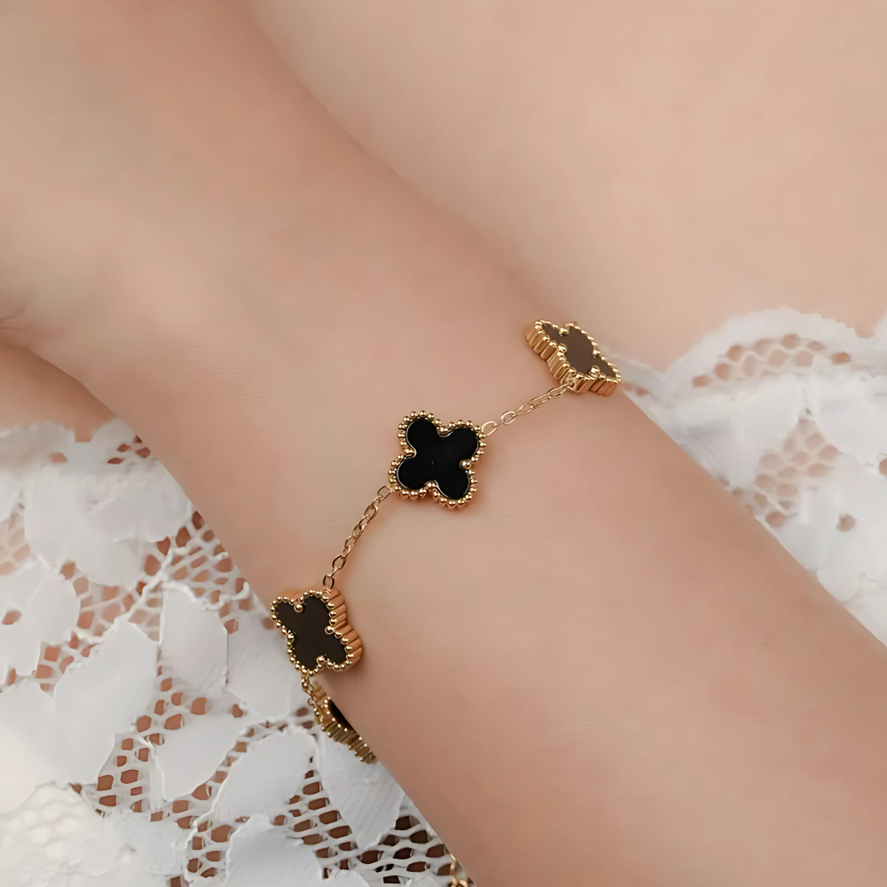 Gold bracelet with black clover charms on a person wearing a white lace garment.