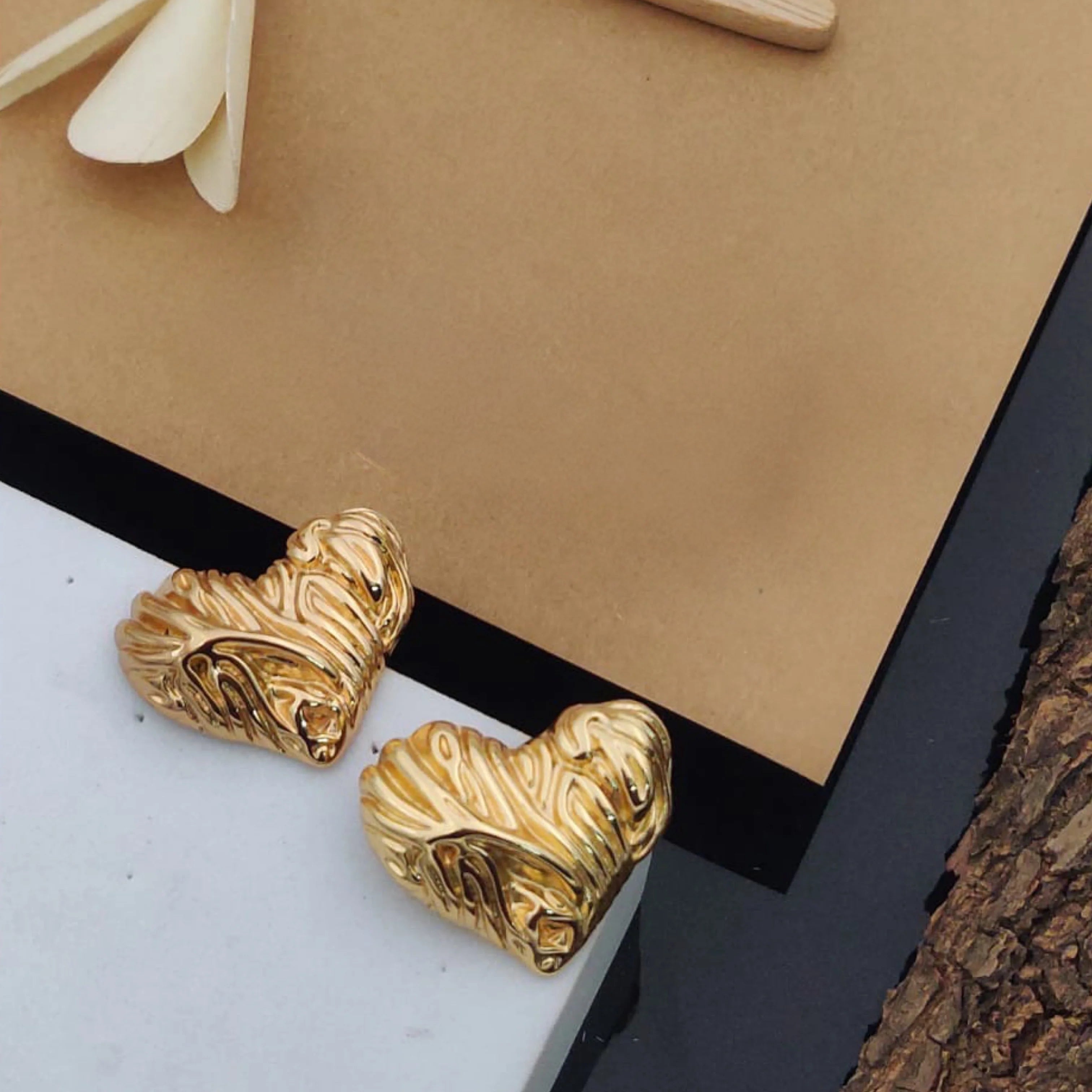 Gold heart-shaped earrings on a marble surface with a beige background